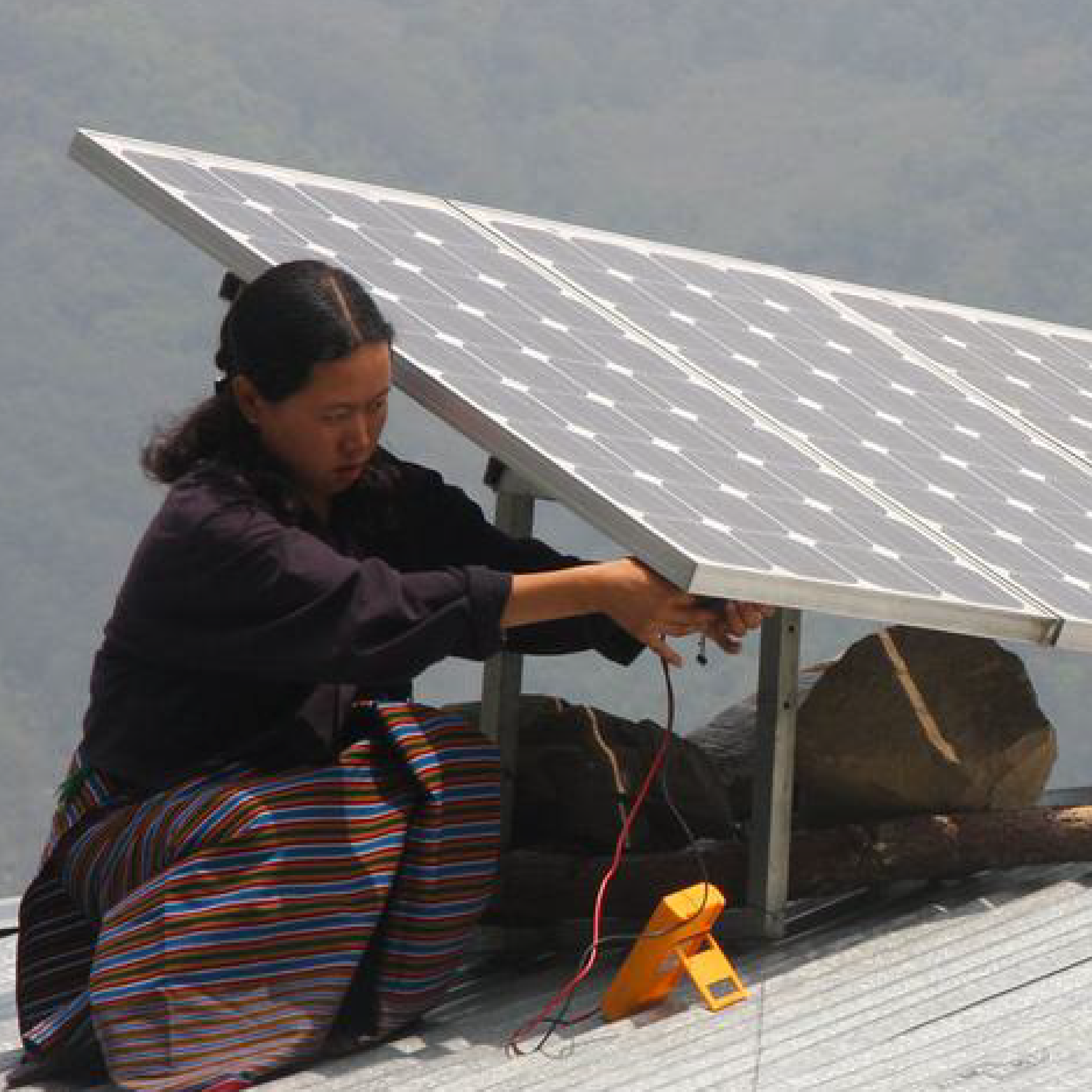 A woman installs a solar panel on a roof in Bhutan.